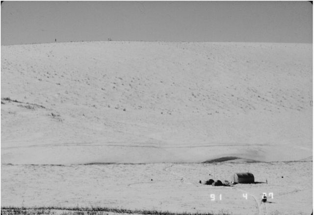 Aerial view of snow-covered hillside with two small tents and one large tent structure in the foreground.